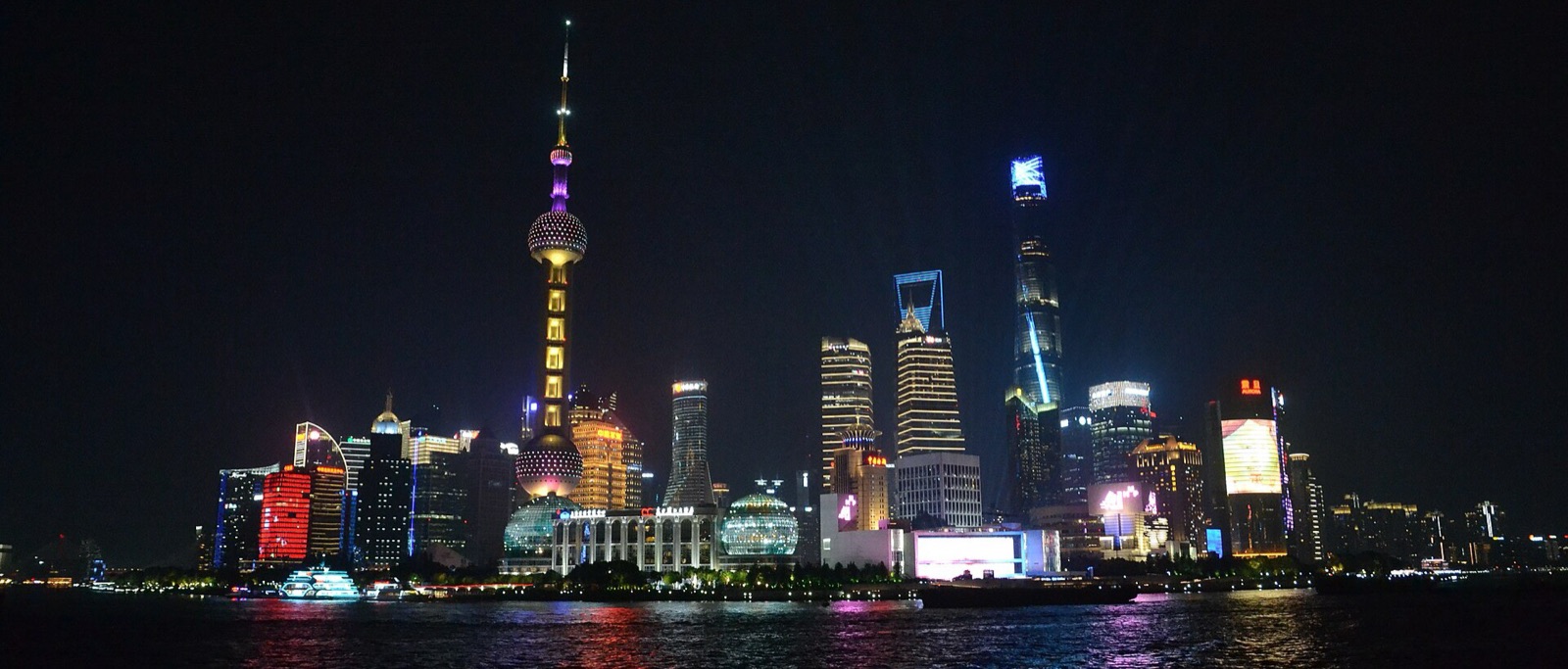 The Lujiazui skyline in Shanghai at night, with the Oriental Pearl Tower and the Shanghai Tower reflected in the Huangpu River
